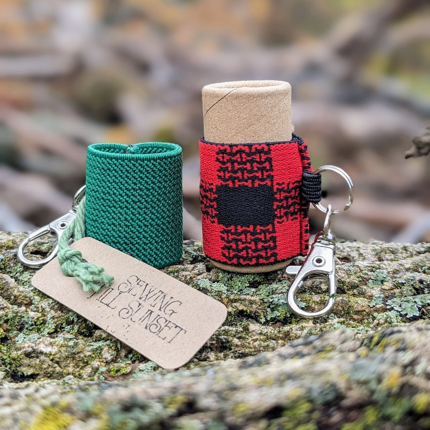Two elastic lip balm holders with keychains, one green and one red and black. On display on a wooden surface.