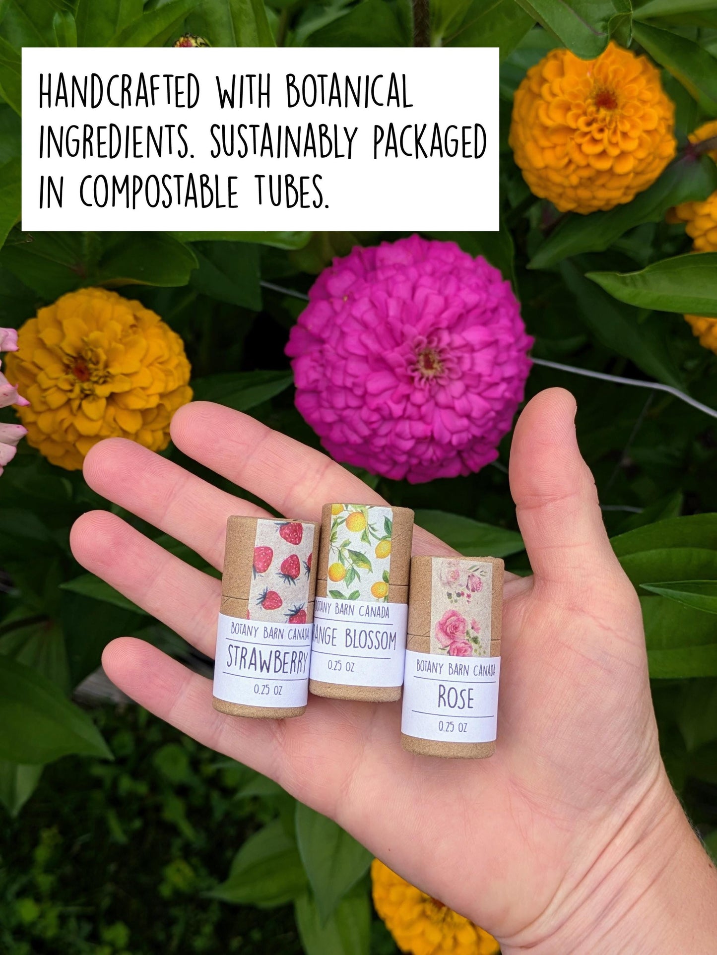 Hand holding three lip balms with colourful labels against a background of flowers.